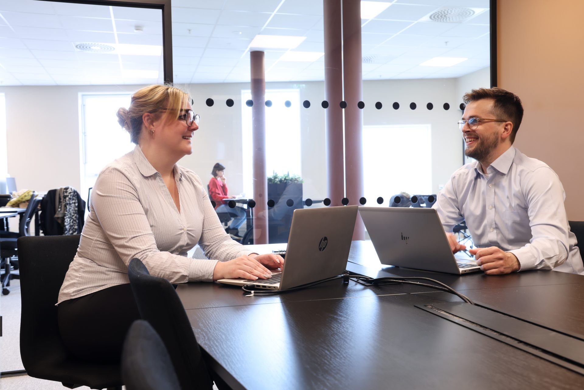 Kvinne og mann sitter ved PC i et møterom