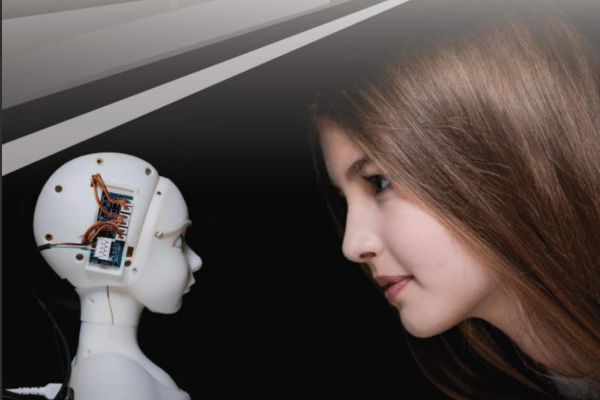 Kvinne med brunt langt hår ser mot et lite hvitt robothode med ledninger som stikker ut fra siden av hodet