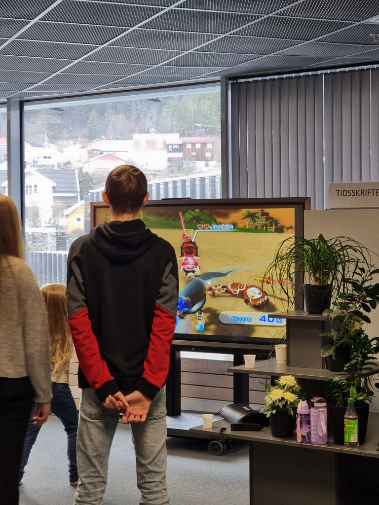 to ungdommer står med ryggen til og ser på storskjerm hvor det spilles tv-spill