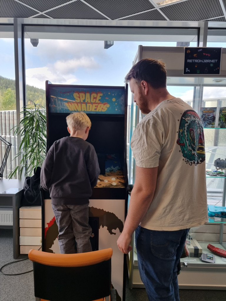 liten gutt spiller på retro spillmaskin mens en voksen mann står ved siden av og følger spent med