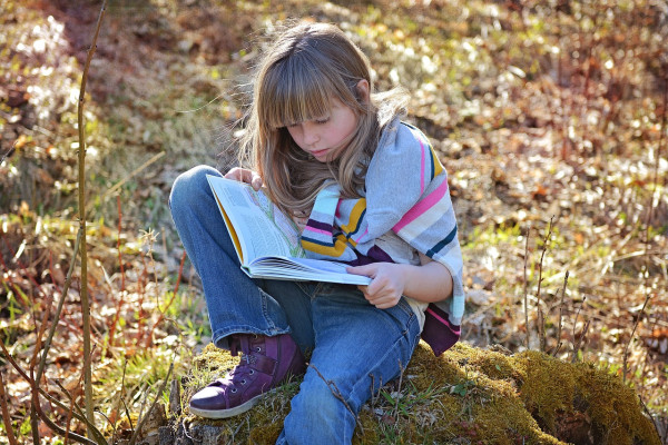 ung jente sitter ute på høstlig skogbunn og leser i bok