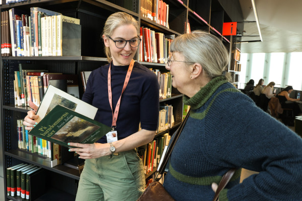 bibliotekar holder bok og veileder besøkende eldre kvinne i biblioteket