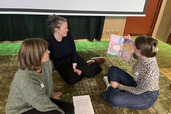 Tre personer sitter på gulvet med en bok.